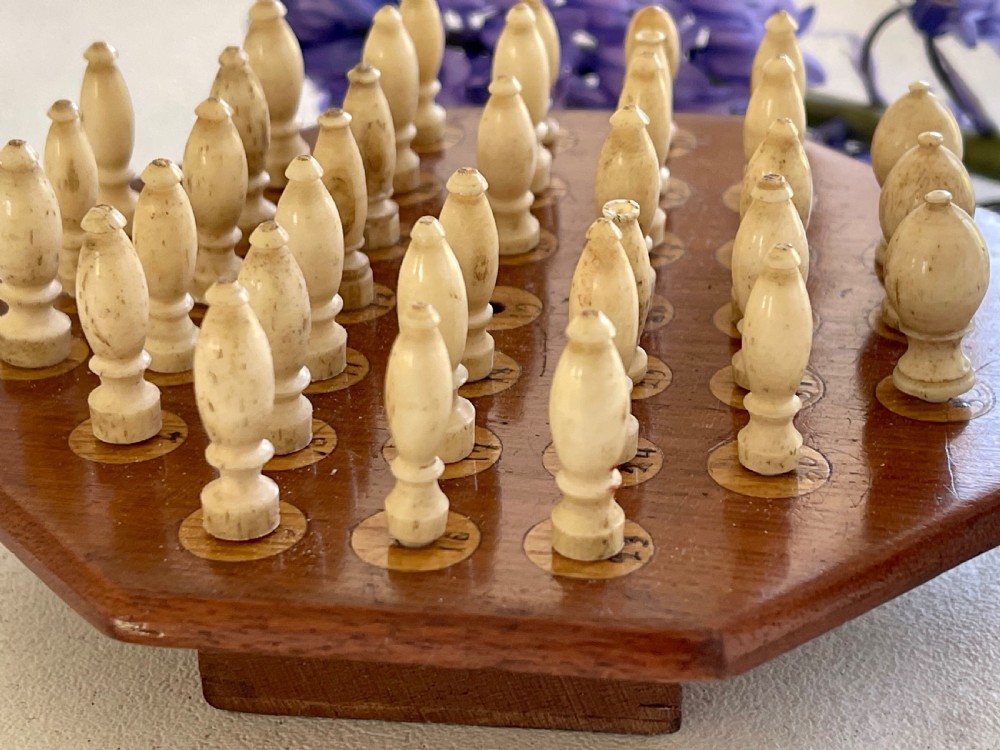 A paddle-shaped wooden peg solitaire board featuring numbered slots and carved bone pegs. View IV