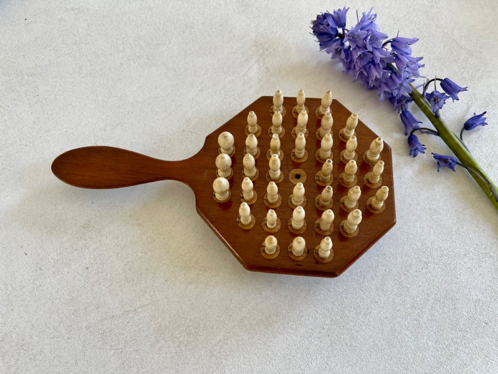 A paddle-shaped wooden peg solitaire board featuring numbered slots and carved bone pegs. View V