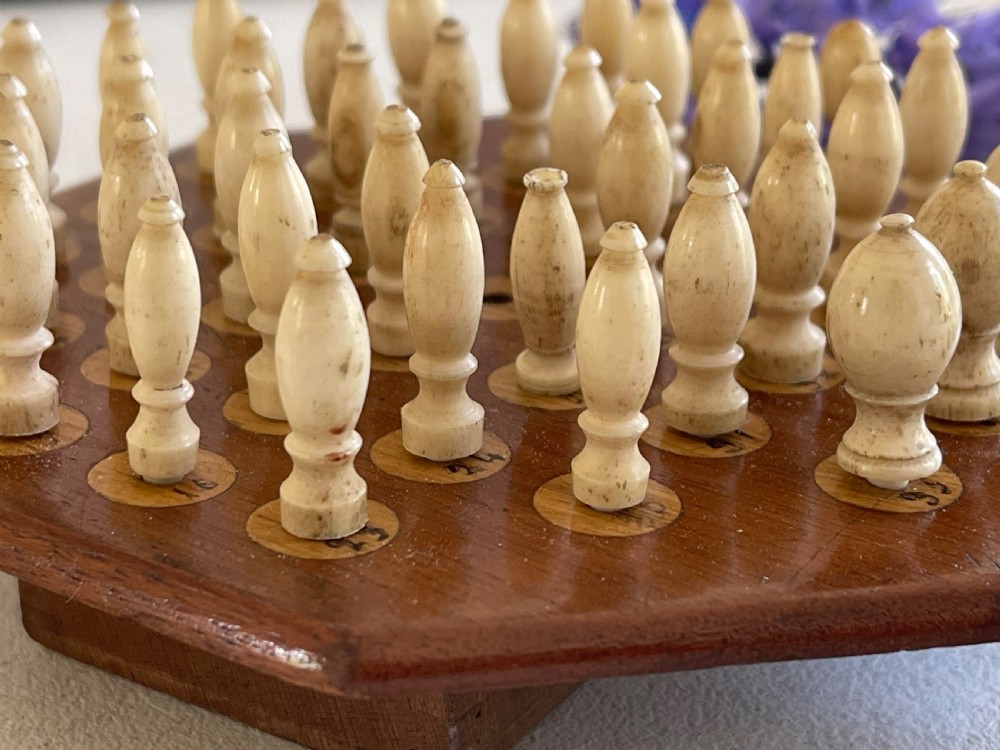 A paddle-shaped wooden peg solitaire board featuring numbered slots and carved bone pegs. View VII