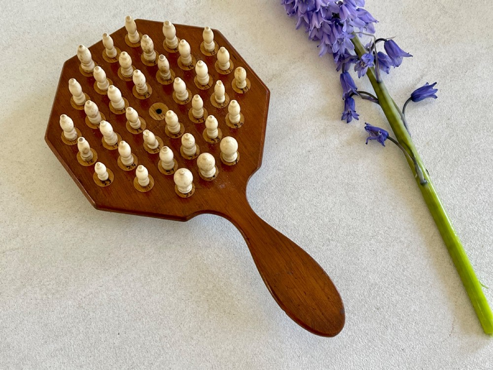 A paddle-shaped wooden peg solitaire board featuring numbered slots and carved bone pegs. View IX
