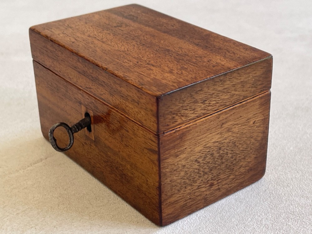 An open small wooden tea caddy featuring two internal compartments with turned knobs, a blue-lined interior lid, and a key inserted into the front lock. View VI