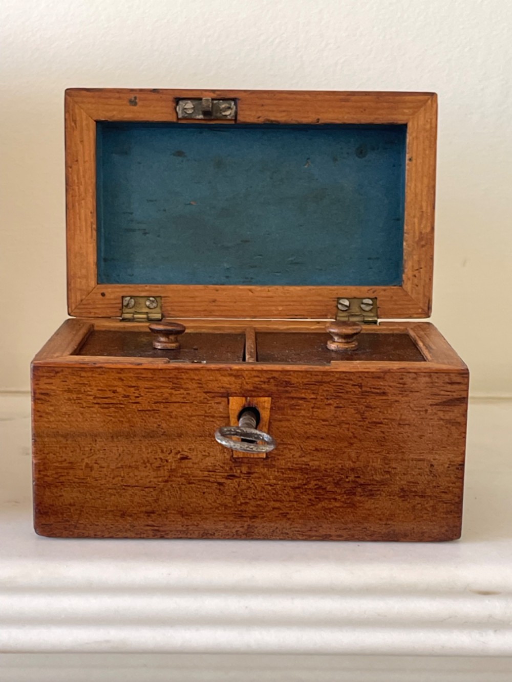 An open small wooden tea caddy featuring two internal compartments with turned knobs, a blue-lined interior lid, and a key inserted into the front lock. View VIII