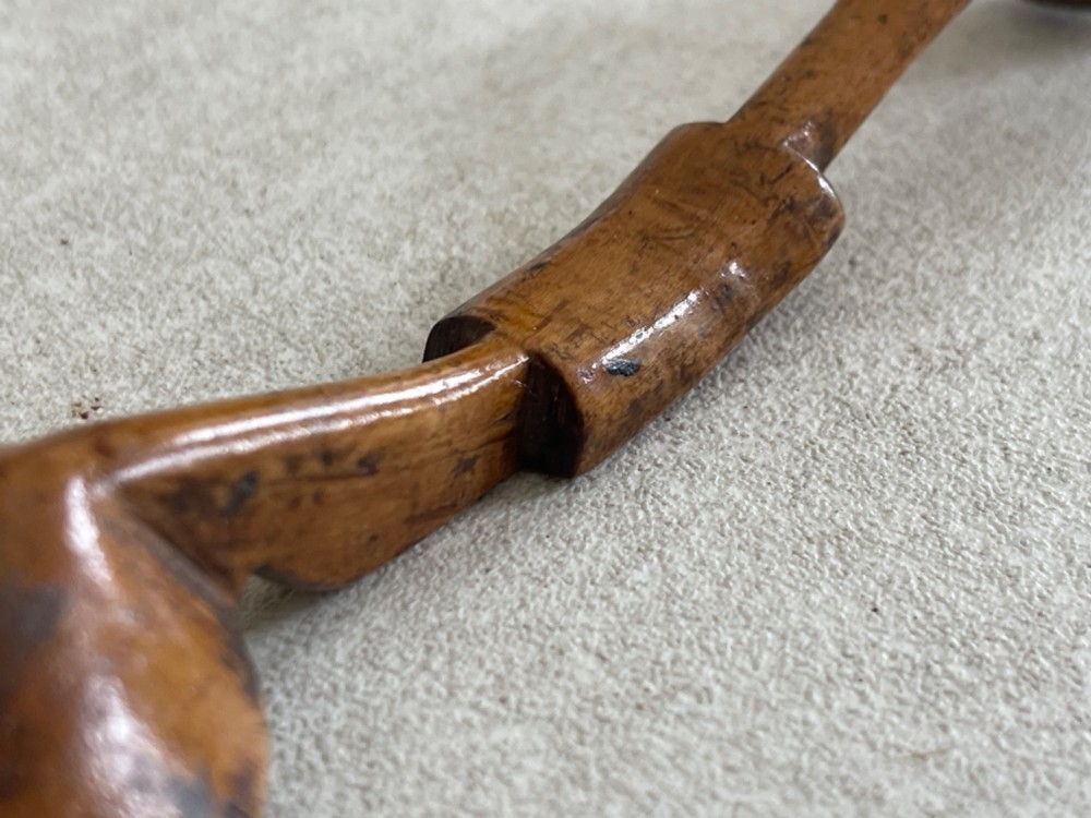A hand-carved antique wooden spoon featuring a shallow pointed bowl, a stepped shaft, and a curved terminal hook. View II