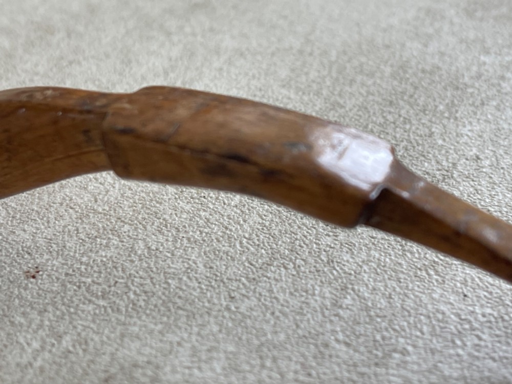 A hand-carved antique wooden spoon featuring a shallow pointed bowl, a stepped shaft, and a curved terminal hook. View III