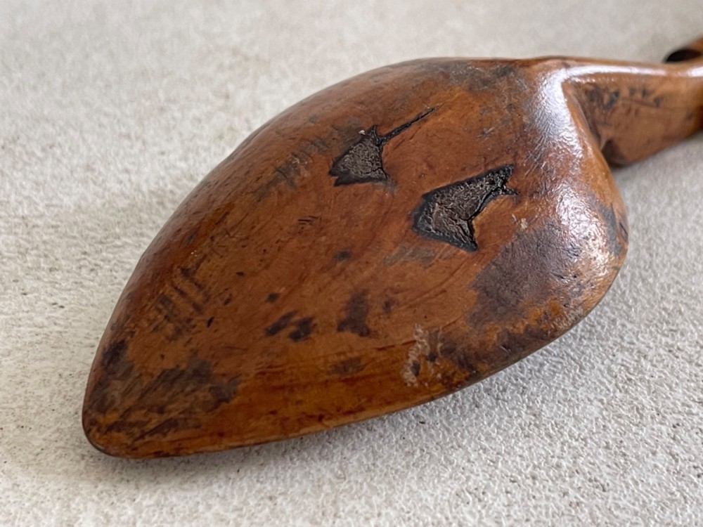 A hand-carved antique wooden spoon featuring a shallow pointed bowl, a stepped shaft, and a curved terminal hook. View IV