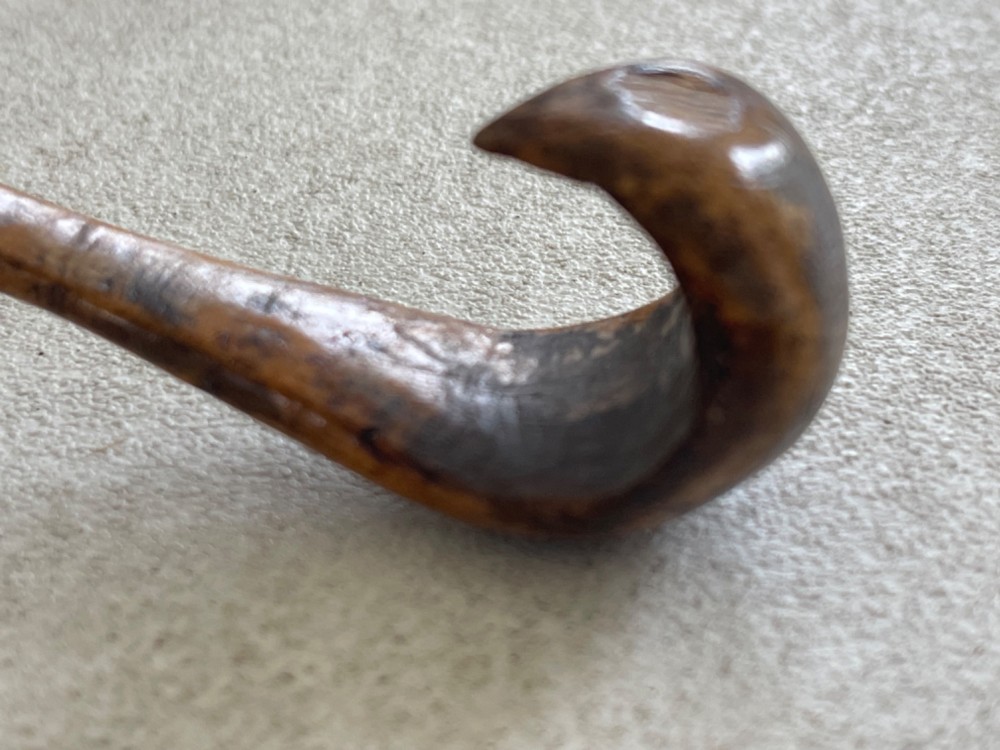 A hand-carved antique wooden spoon featuring a shallow pointed bowl, a stepped shaft, and a curved terminal hook. View V