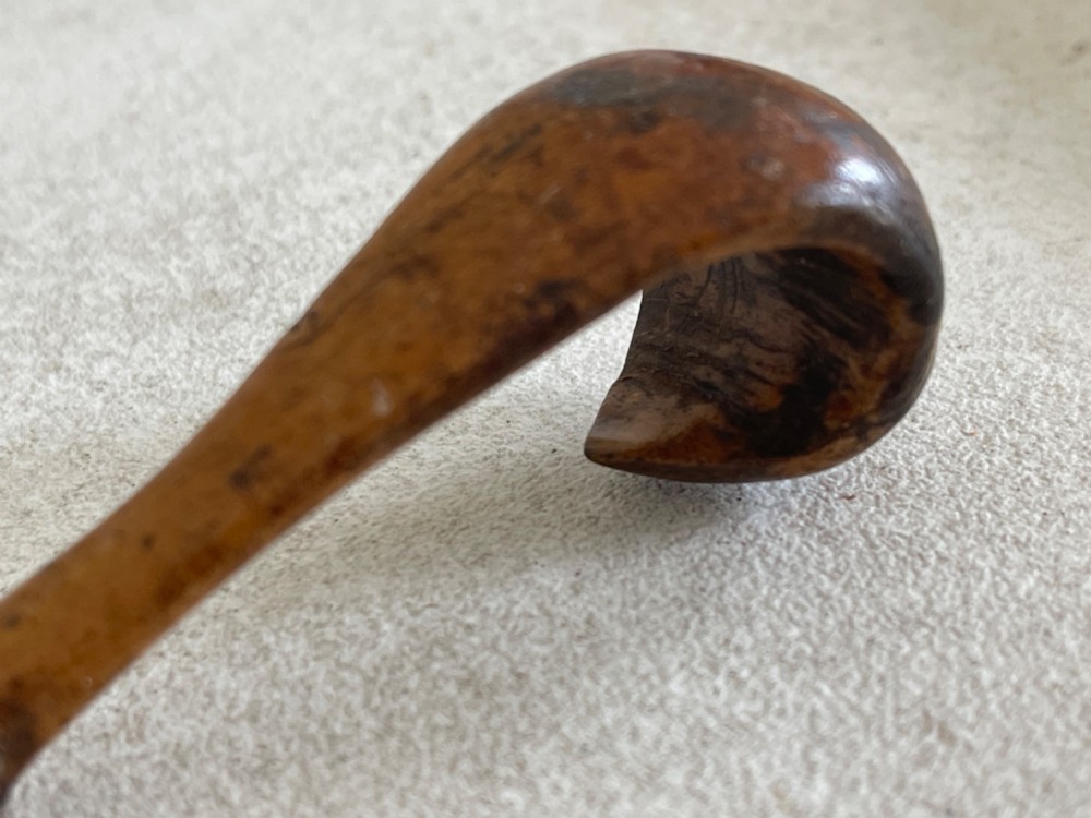 A hand-carved antique wooden spoon featuring a shallow pointed bowl, a stepped shaft, and a curved terminal hook. View VI