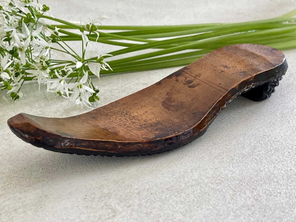 A carved wooden knitting sheath crafted in the shape of a shoe sole with a polished dark surface.