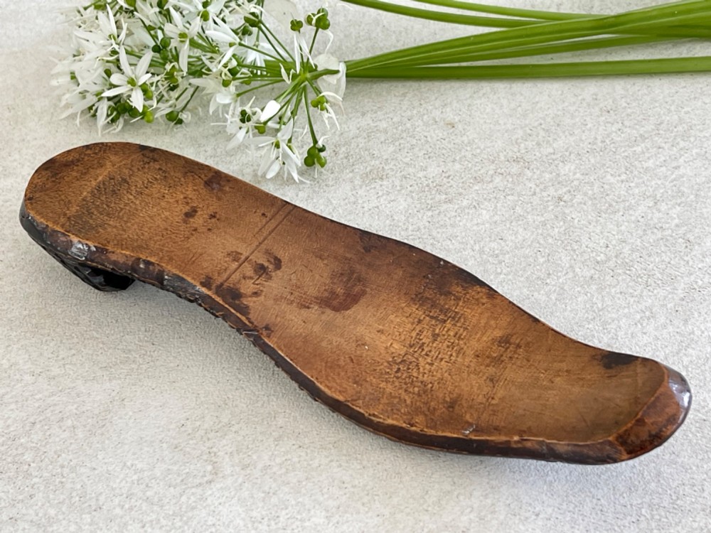 A carved wooden knitting sheath crafted in the shape of a shoe sole with a polished dark surface. View II
