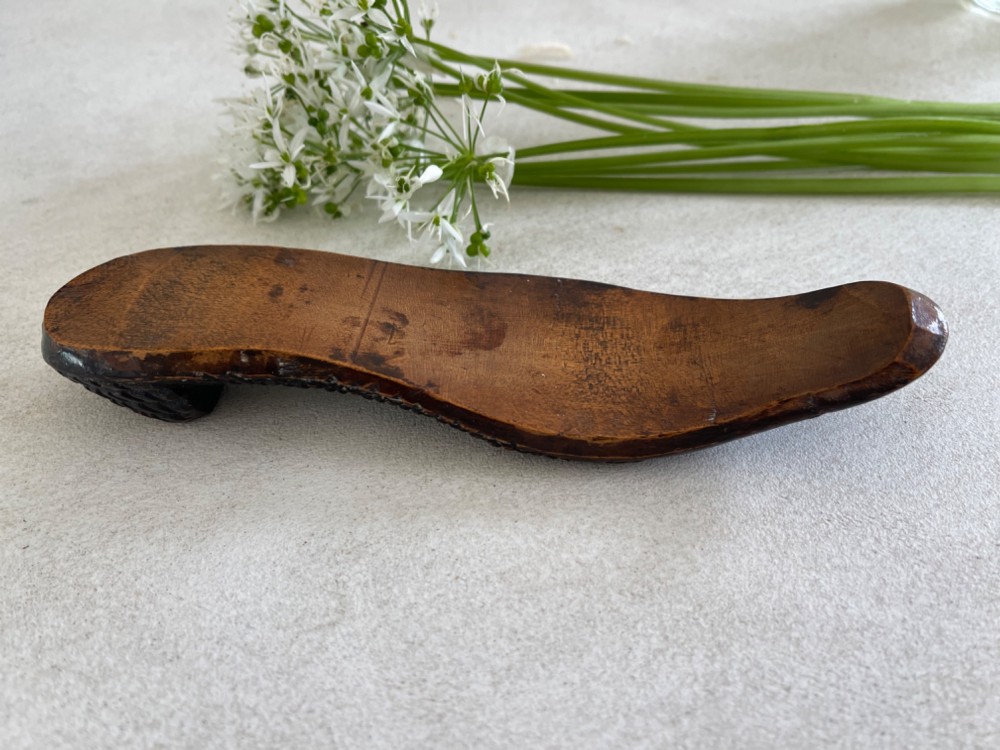 A carved wooden knitting sheath crafted in the shape of a shoe sole with a polished dark surface. View III