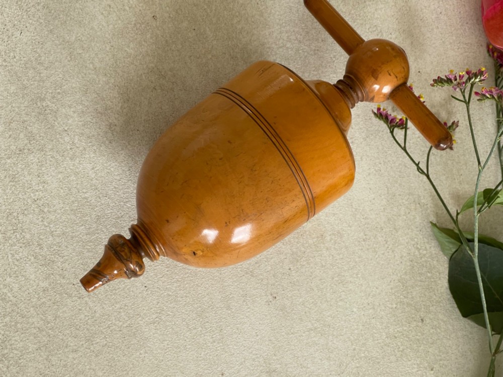 A turned wooden urn-shaped lemon squeezer with a threaded screw handle and spout tip in a warm amber finish.