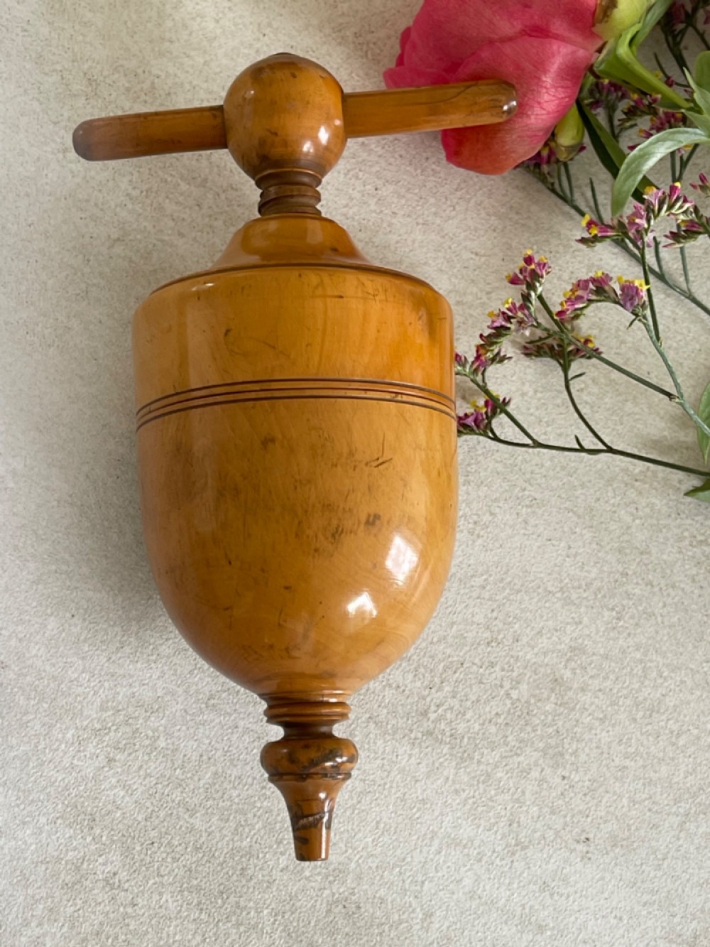 A turned wooden urn-shaped lemon squeezer with a threaded screw handle and spout tip in a warm amber finish. View III