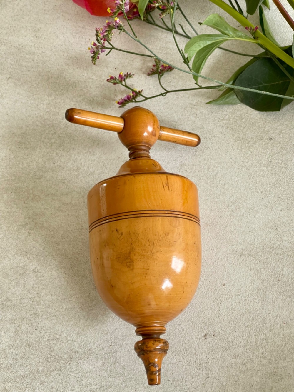 A turned wooden urn-shaped lemon squeezer with a threaded screw handle and spout tip in a warm amber finish. View IV