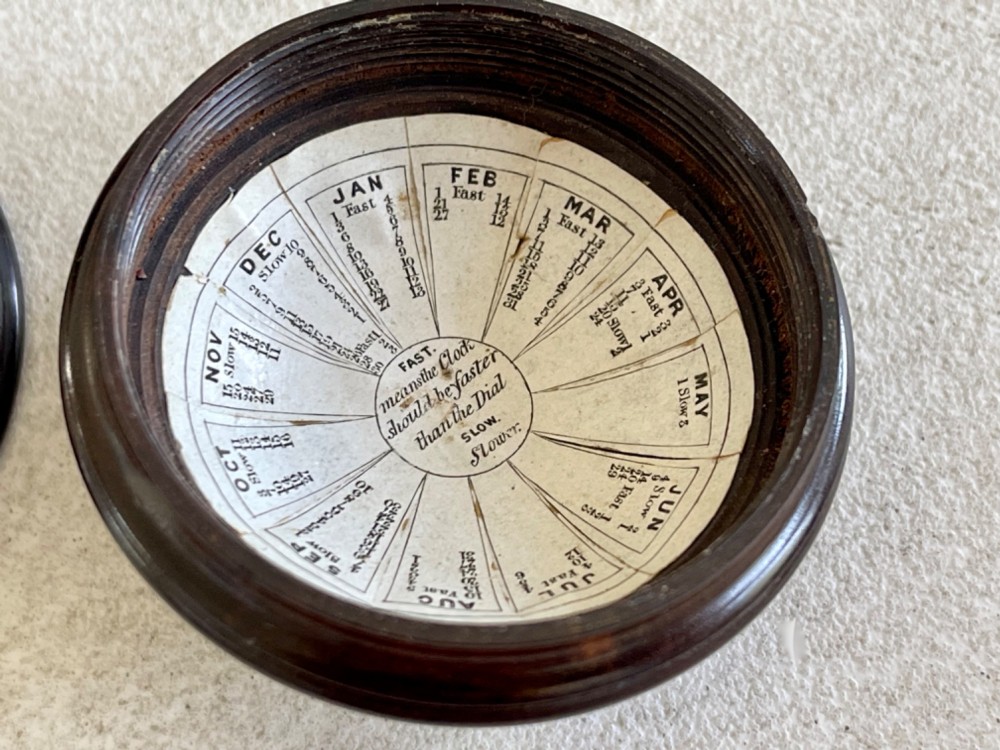 A turned dark lignum vitae wooden case opening to reveal a pocket compass and solar sundial beneath a domed glass lens. View III