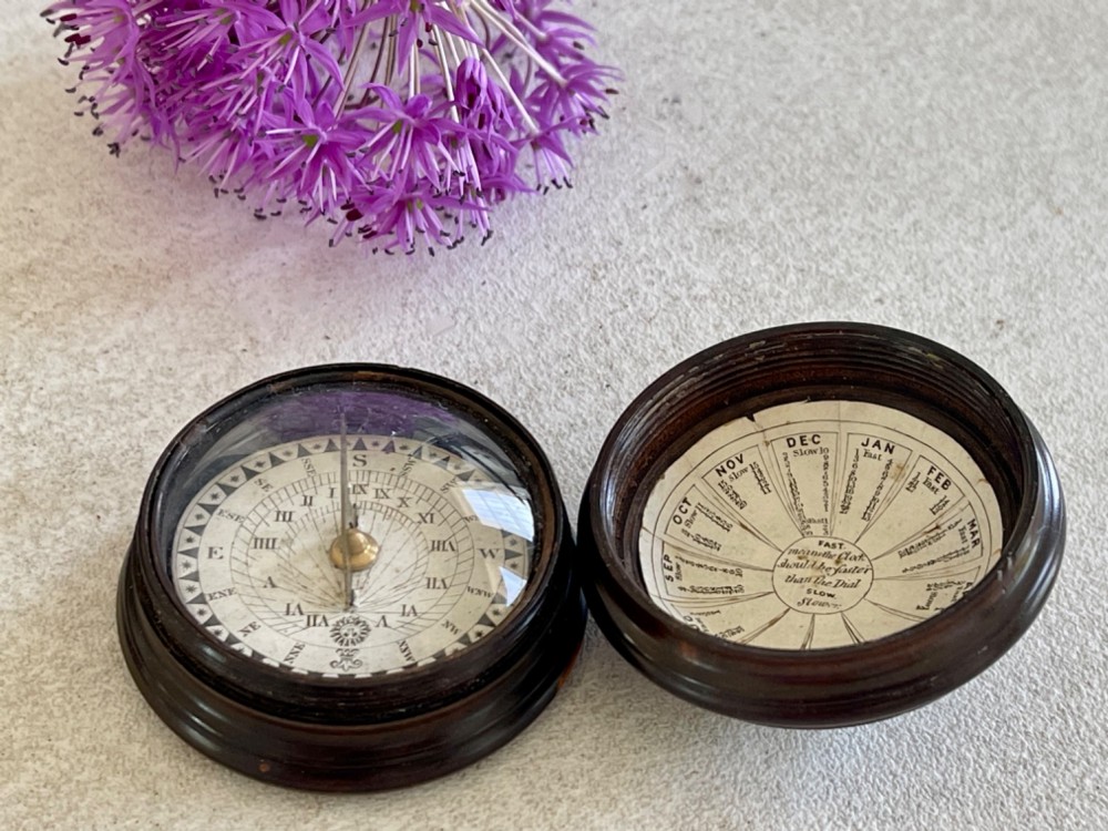 A turned dark lignum vitae wooden case opening to reveal a pocket compass and solar sundial beneath a domed glass lens. View IV