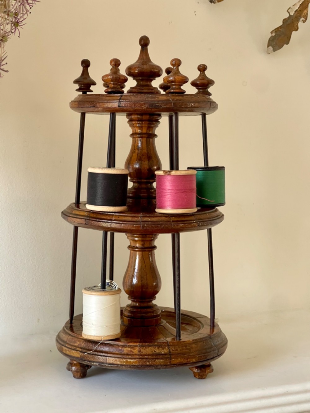 A multi-tiered turned wooden cotton reel stand with vertical metal spindles holding coloured spools of thread on bun feet.