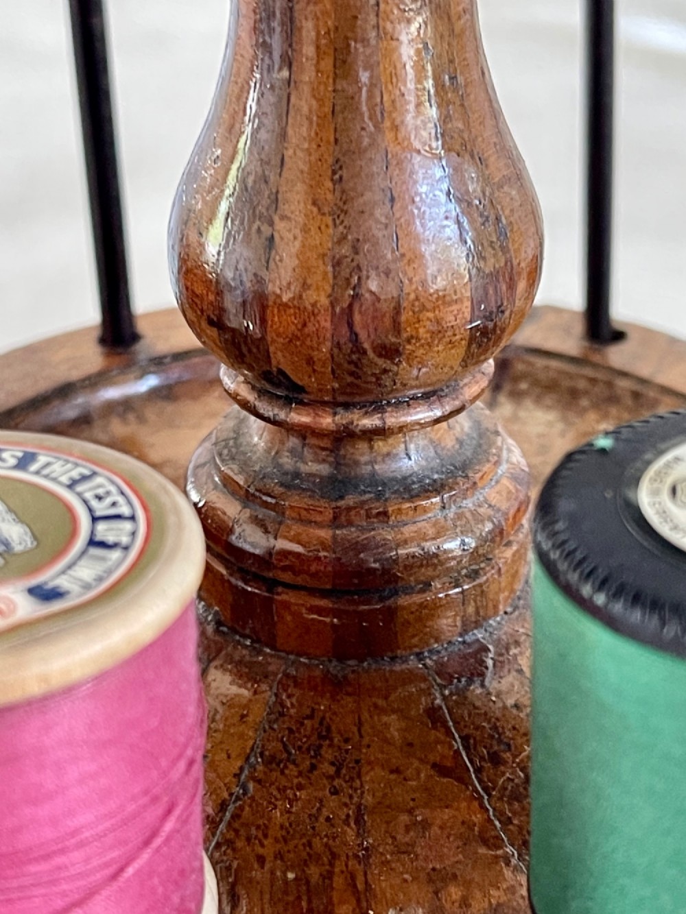 A multi-tiered turned wooden cotton reel stand with vertical metal spindles holding coloured spools of thread on bun feet. View II