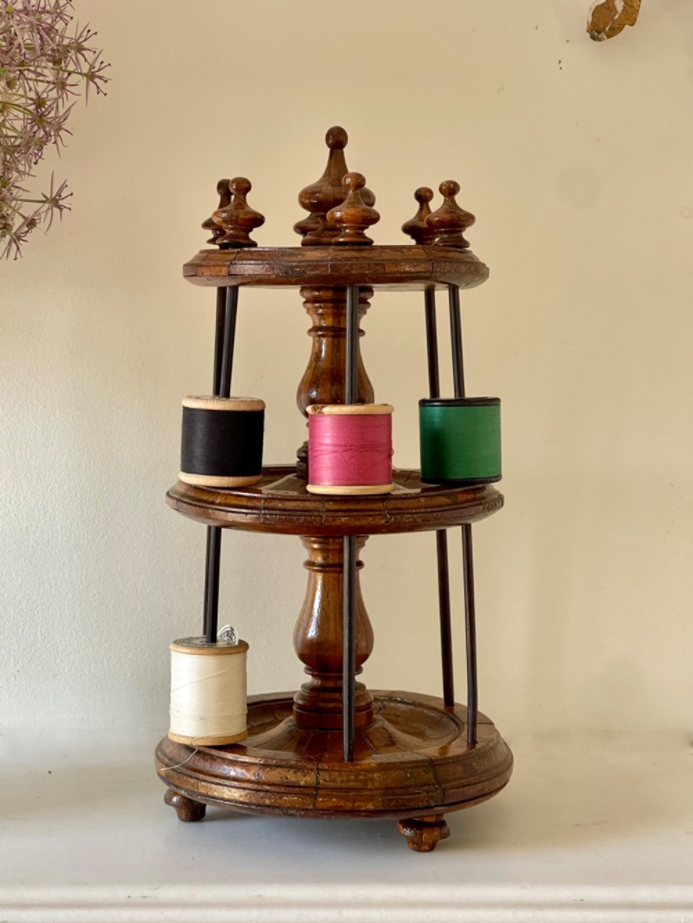 A multi-tiered turned wooden cotton reel stand with vertical metal spindles holding coloured spools of thread on bun feet. View III