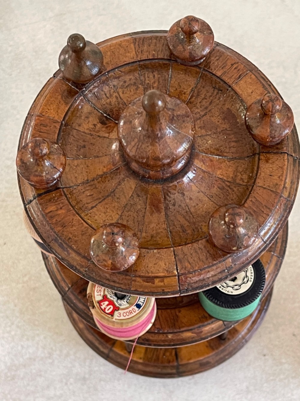 A multi-tiered turned wooden cotton reel stand with vertical metal spindles holding coloured spools of thread on bun feet. View IV