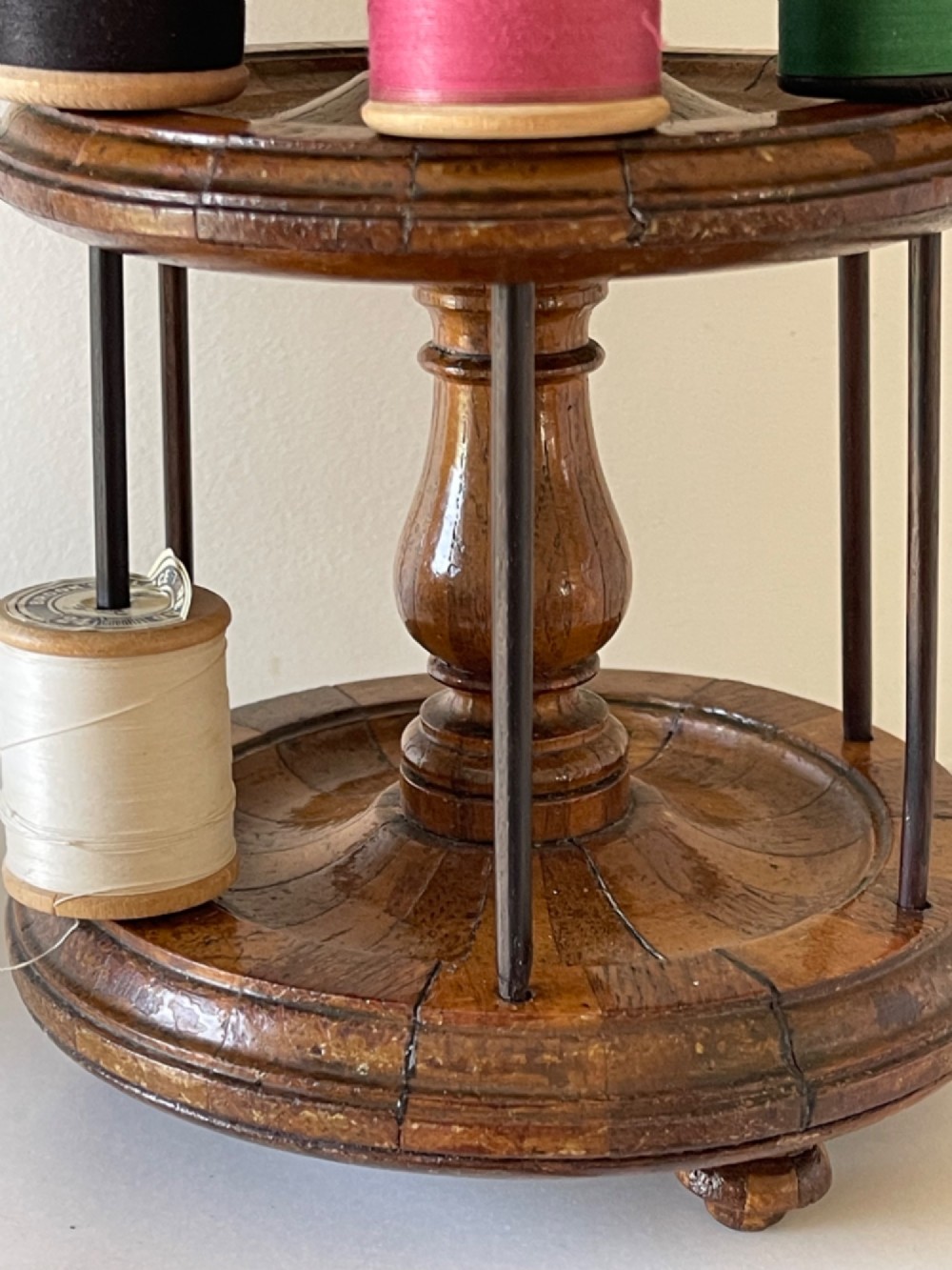 A multi-tiered turned wooden cotton reel stand with vertical metal spindles holding coloured spools of thread on bun feet. View VI
