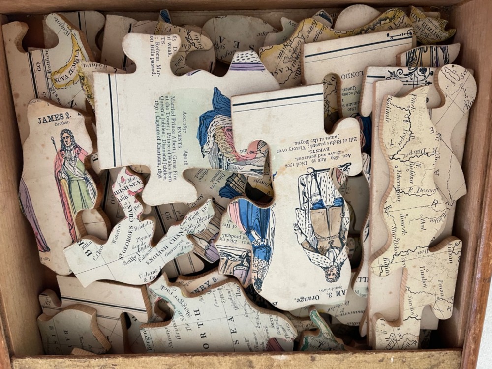 An antique wooden box featuring a printed paper label titled Peacocks New Double Dissection Geography and History England and Wales with illustrations of a globe, historical figures, and coat of arms. View II