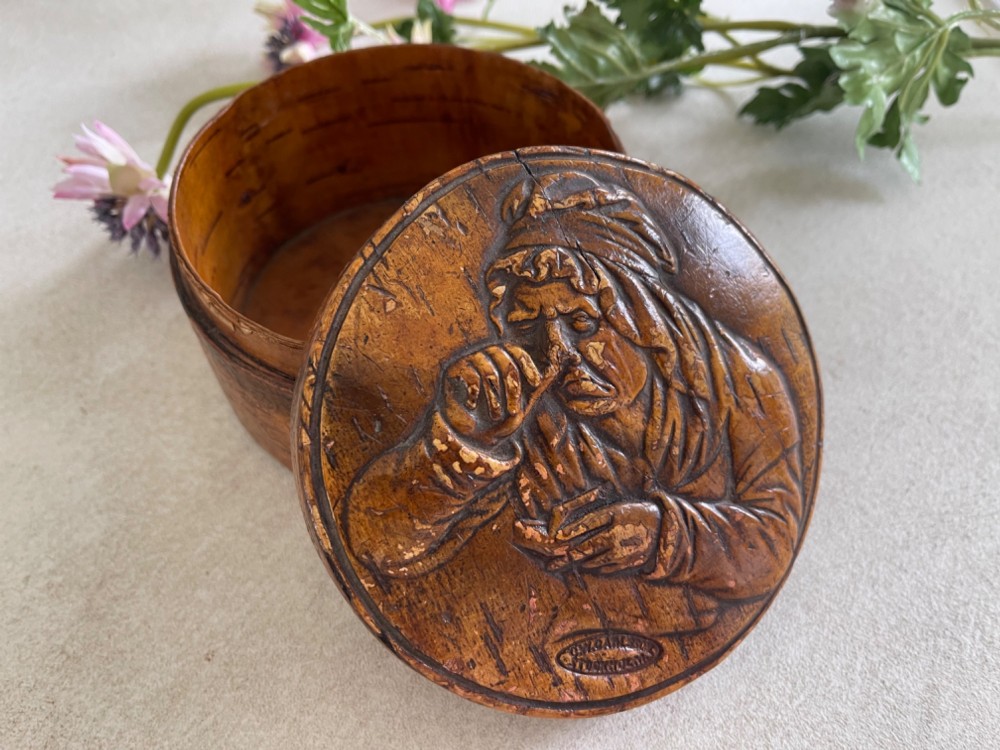 A circular brown wooden table snuff box lid decorated with a relief illustration depicting a figure taking snuff and a stamped maker mark. View IV