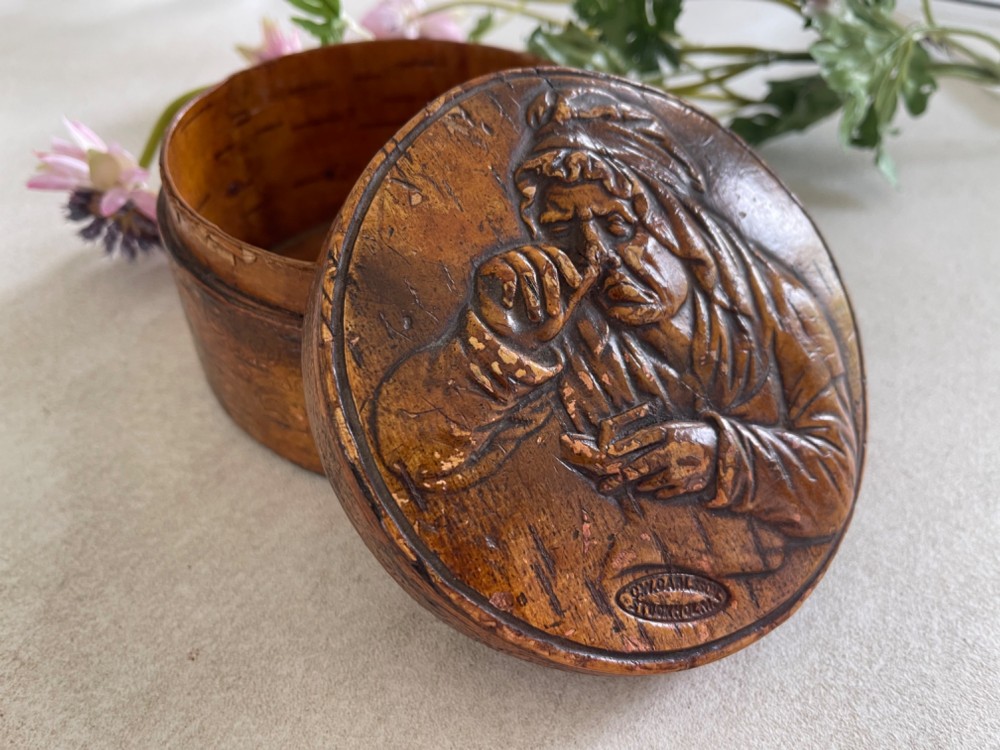 A circular brown wooden table snuff box lid decorated with a relief illustration depicting a figure taking snuff and a stamped maker mark. View VI