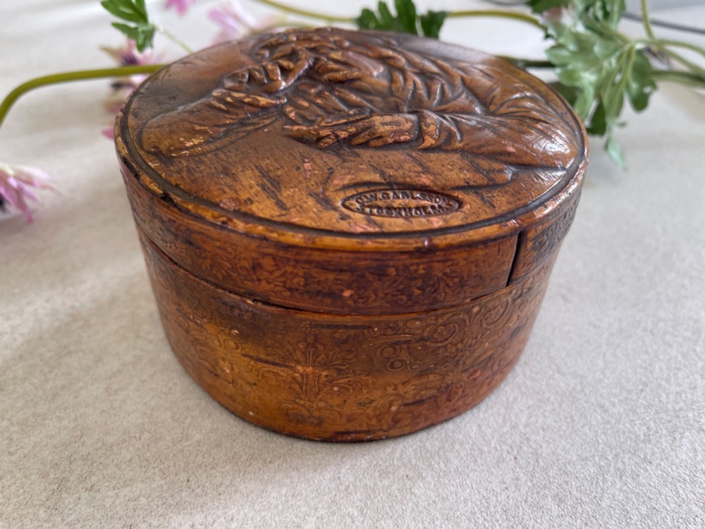 A circular brown wooden table snuff box lid decorated with a relief illustration depicting a figure taking snuff and a stamped maker mark. View VIII