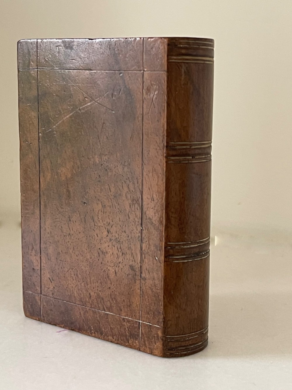 A small warm brown wooden box shaped to resemble a bound book with a silver shield cartouche inlaid on the front lid. View III