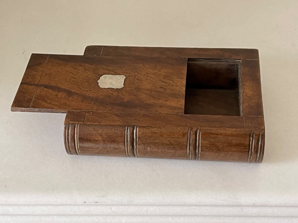 A small warm brown wooden box shaped to resemble a bound book with a silver shield cartouche inlaid on the front lid. View IV