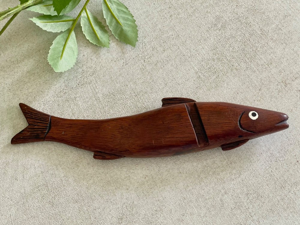 A hand-carved dark wood knitting sheath shaped like a fish, featuring an inlaid eye and carved initials near the tail fin. View II