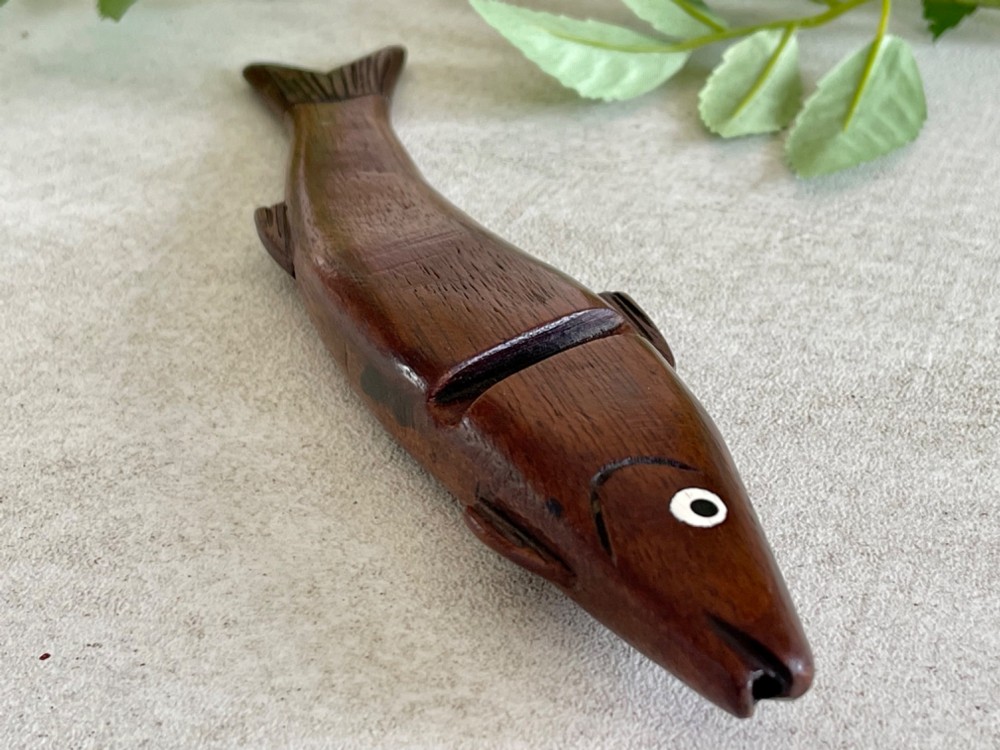 A hand-carved dark wood knitting sheath shaped like a fish, featuring an inlaid eye and carved initials near the tail fin. View III