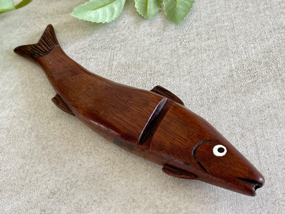 A hand-carved dark wood knitting sheath shaped like a fish, featuring an inlaid eye and carved initials near the tail fin. View IV