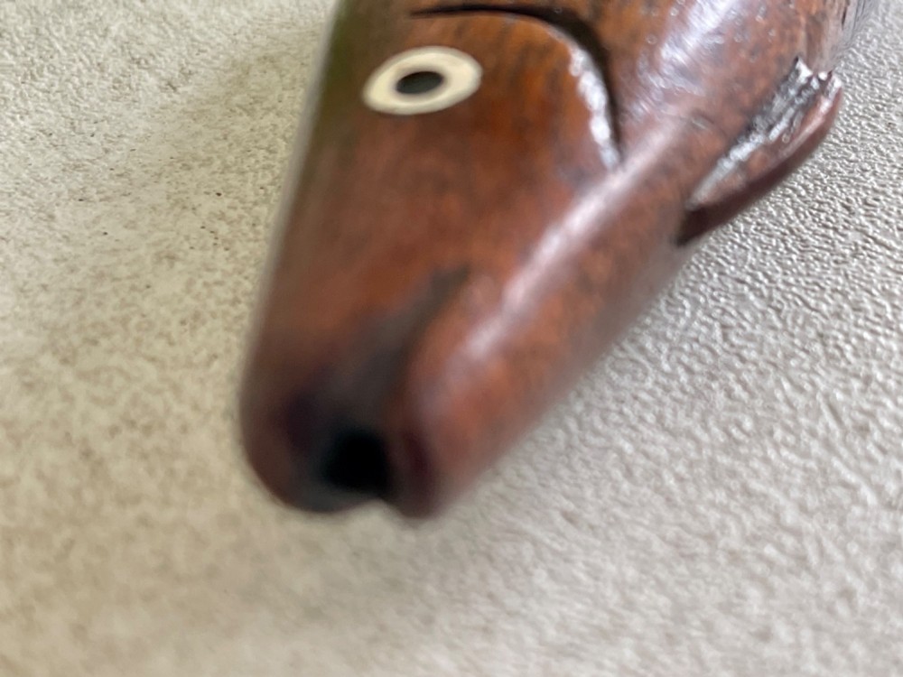 A hand-carved dark wood knitting sheath shaped like a fish, featuring an inlaid eye and carved initials near the tail fin. View VI