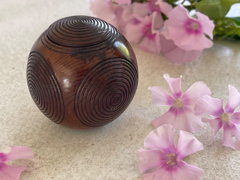 A spherical carved dark brown wooden puzzle ball featuring concentric circular grooves on its outer surface.