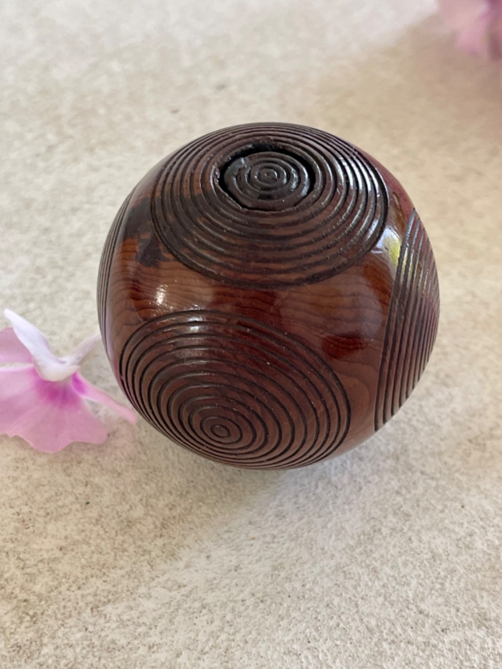 A spherical carved dark brown wooden puzzle ball featuring concentric circular grooves on its outer surface. View V