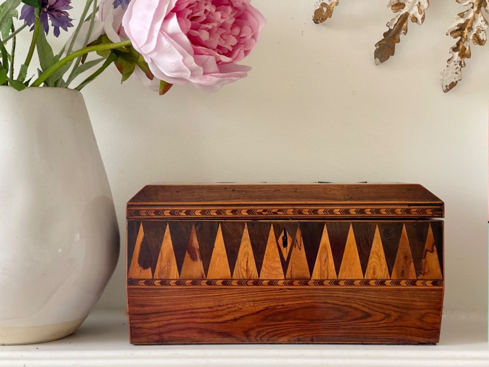 A rectangular Georgian wooden tea caddy featuring geometric triangular parquetry inlay across the front facade and a bevelled lid with a keyhole escutcheon.