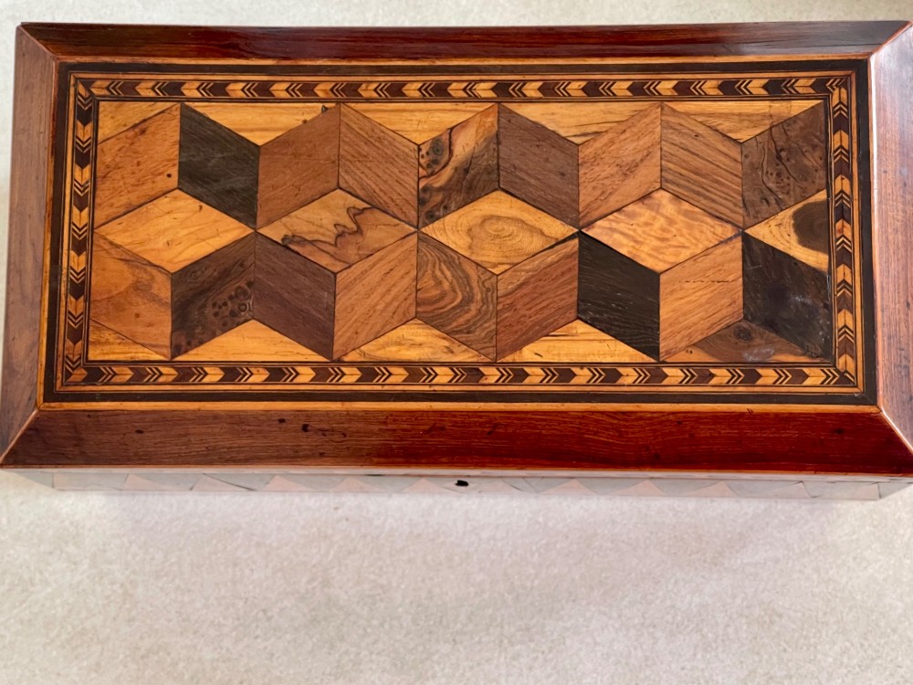 A rectangular Georgian wooden tea caddy featuring geometric triangular parquetry inlay across the front facade and a bevelled lid with a keyhole escutcheon. View III