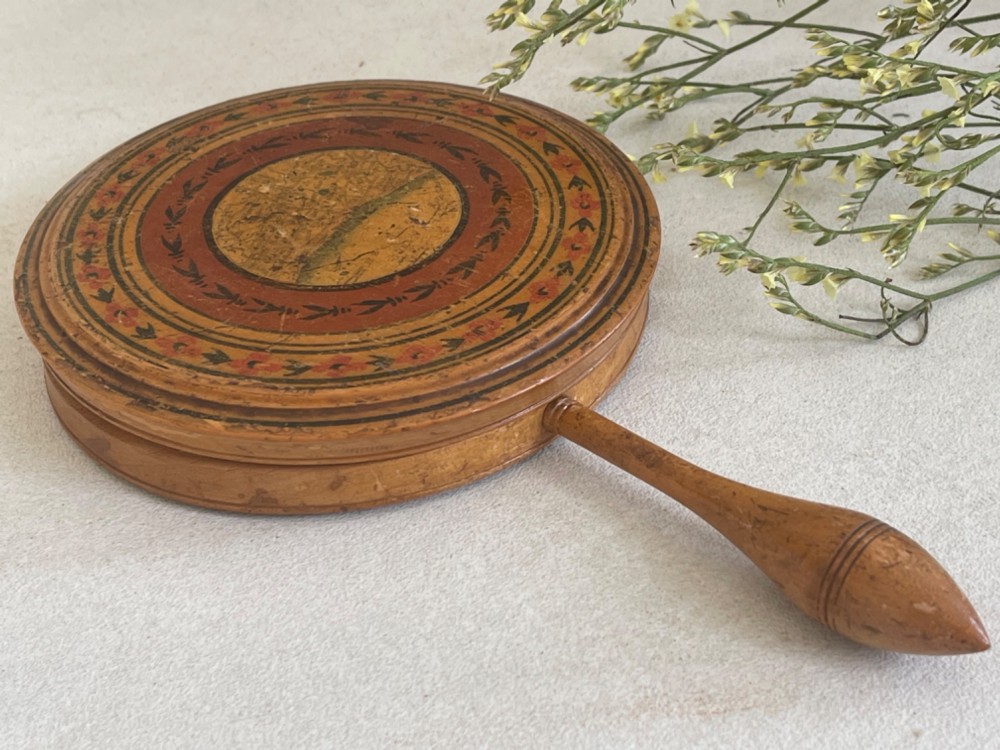 A circular wooden travelling mirror featuring concentric red and black decorative bands around the lid and a turned wood handle.