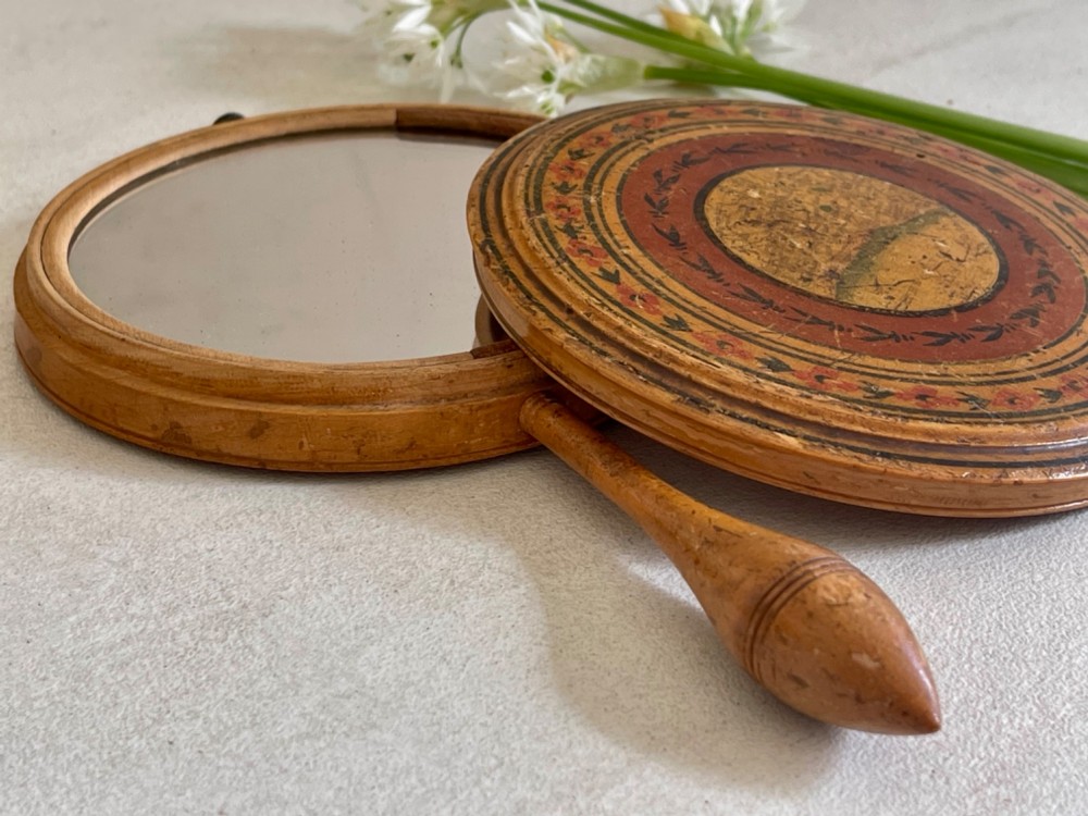 A circular wooden travelling mirror featuring concentric red and black decorative bands around the lid and a turned wood handle. View II