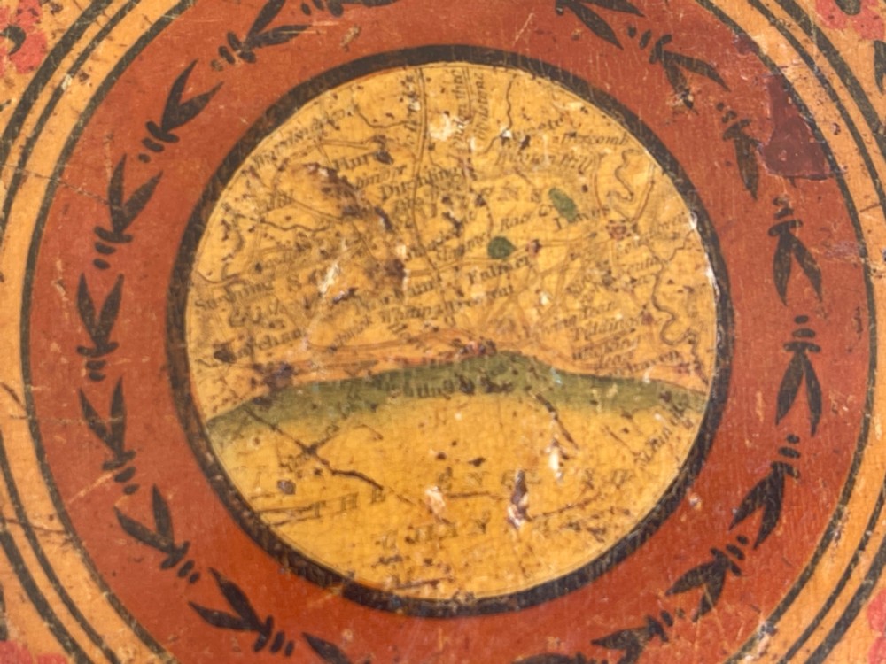 A circular wooden travelling mirror featuring concentric red and black decorative bands around the lid and a turned wood handle. View III