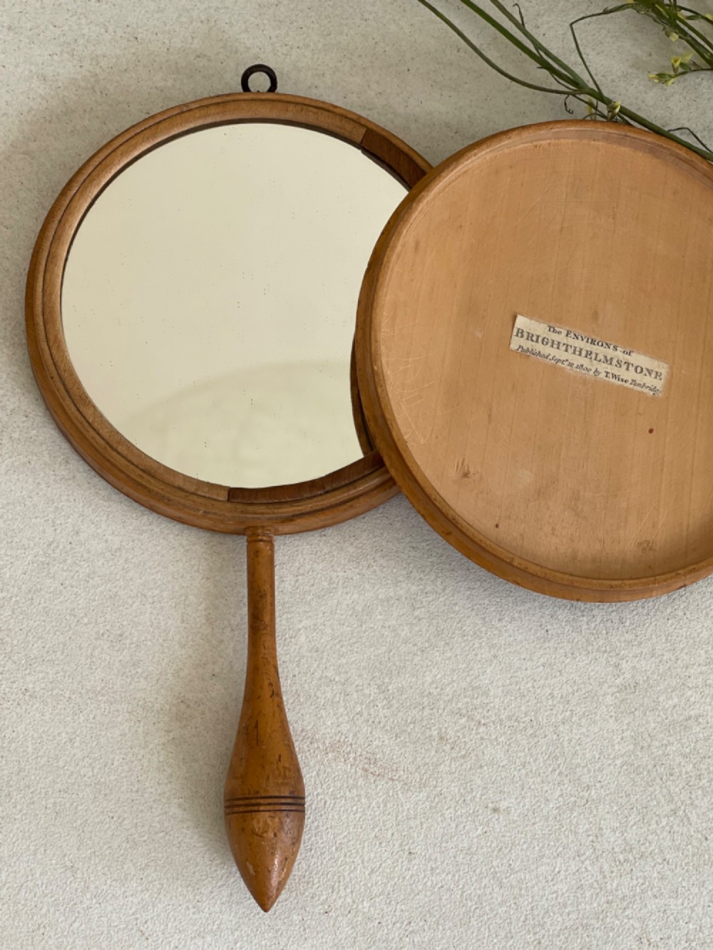 A circular wooden travelling mirror featuring concentric red and black decorative bands around the lid and a turned wood handle. View IV