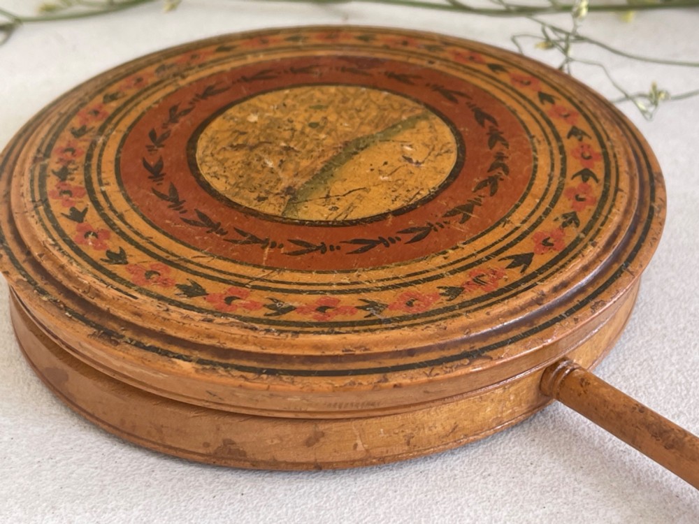 A circular wooden travelling mirror featuring concentric red and black decorative bands around the lid and a turned wood handle. View VIII