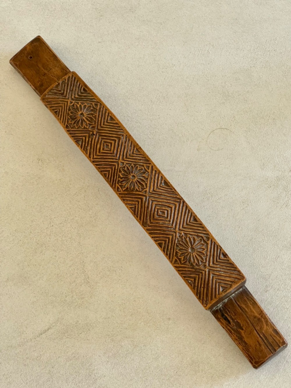 A narrow, elongated carved wooden press mould featuring repeating geometric diamond and rosette patterns in a warm brown finish.