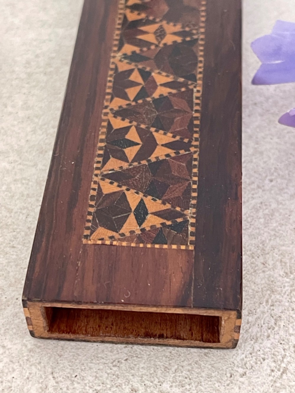 A long rectangular dark rosewood silk skein holder featuring a central band of intricate geometric tessellated wood inlay. View V