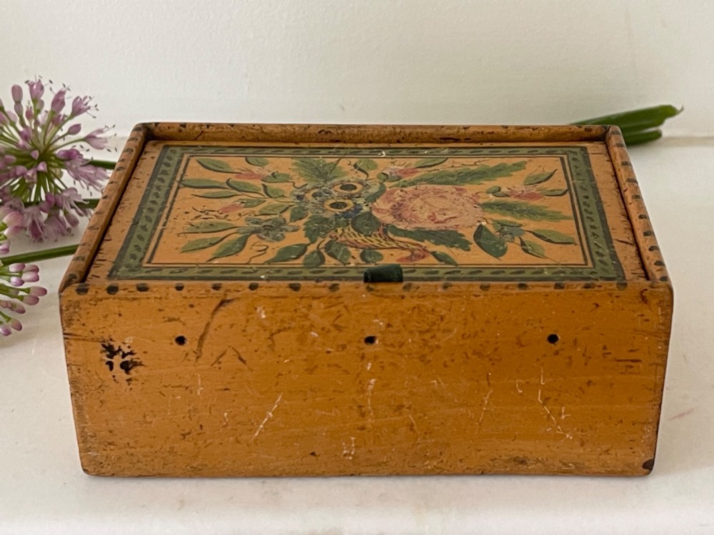 An antique Georgian wooden reel box painted in warm ochre with a floral motif on the lid and thread apertures along the front.