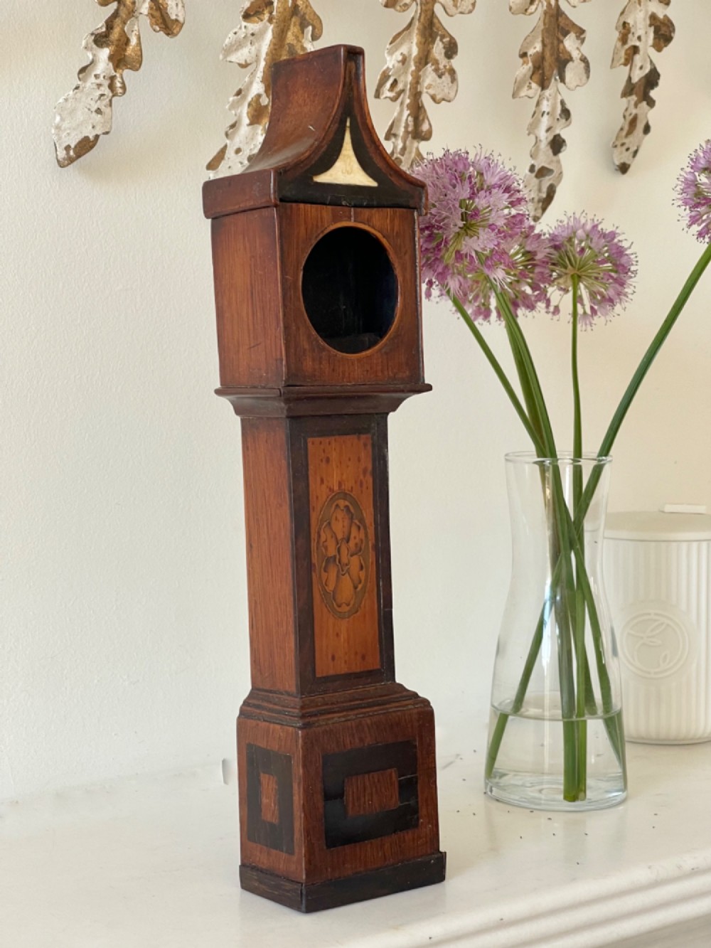 A Georgian treen pocket watch holder shaped as a miniature longcase clock with mahogany timber and floral marquetry inlay. View II