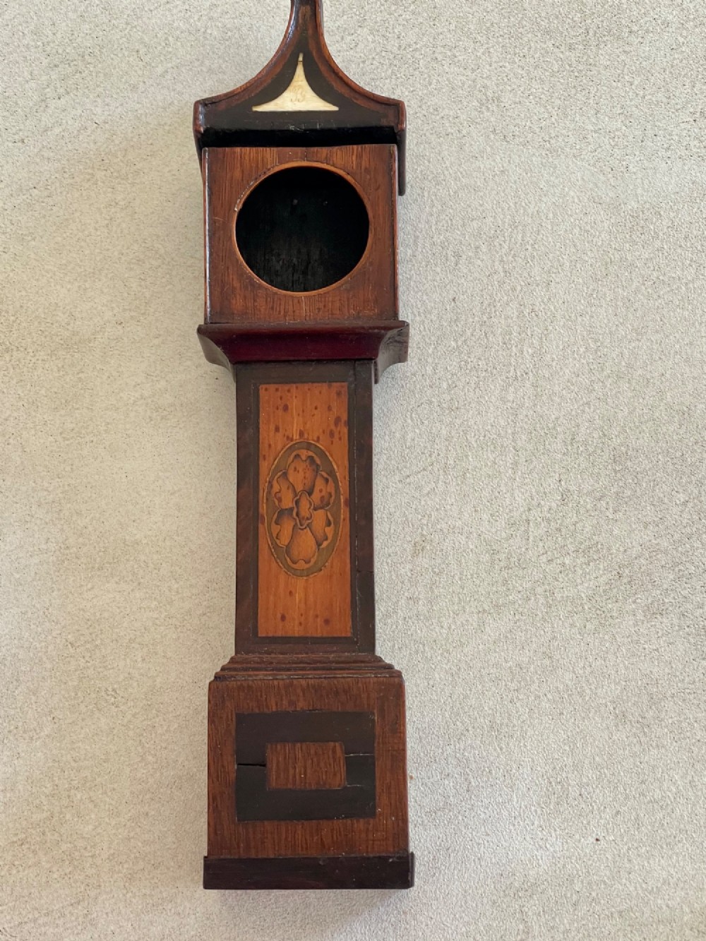 A Georgian treen pocket watch holder shaped as a miniature longcase clock with mahogany timber and floral marquetry inlay. View VI