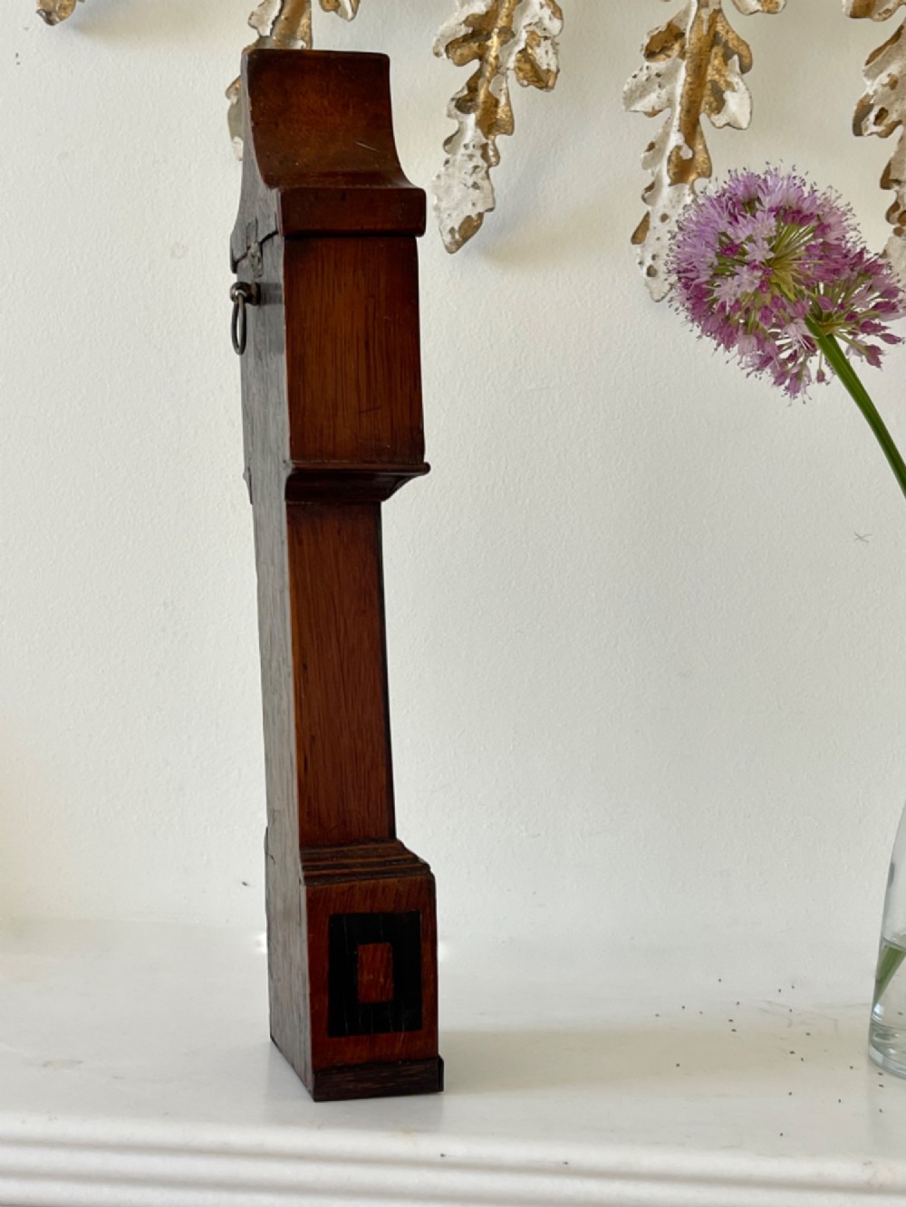 A Georgian treen pocket watch holder shaped as a miniature longcase clock with mahogany timber and floral marquetry inlay. View IX
