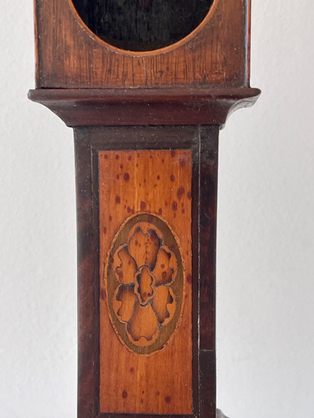 A Georgian treen pocket watch holder shaped as a miniature longcase clock with mahogany timber and floral marquetry inlay. View X